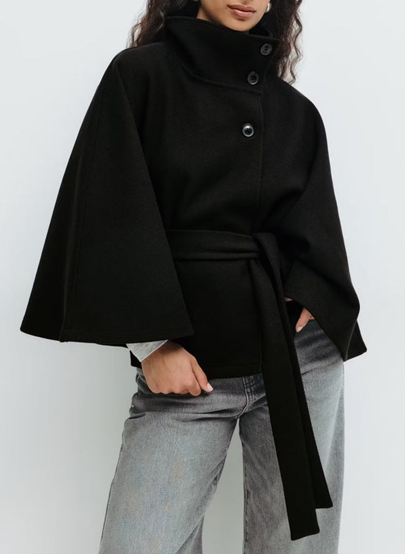 Cape noire ceinturée portée avec un jean gris