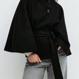 Cape noire ceinturée portée avec un jean gris